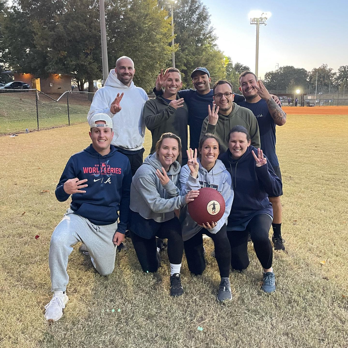 A group of employees posing with a kickball on a field representing the Sagepath kickball team and highlighting company culture.