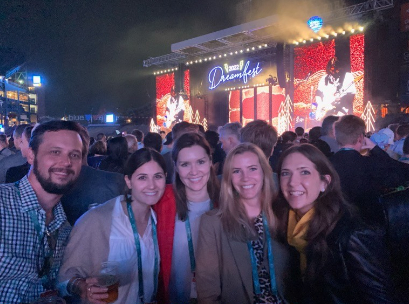 Five people smiling at the 2022 Dreamfest event, with a large outdoor stage and live performance in the background.