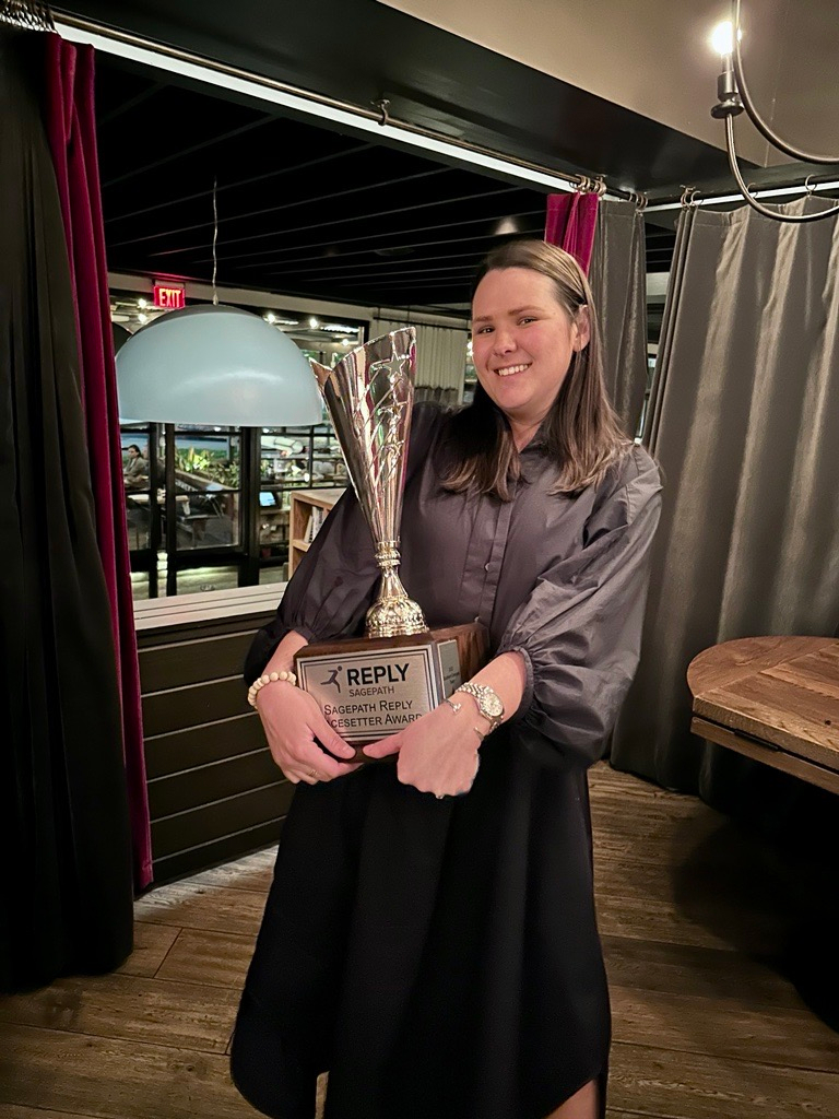 A woman holding the Sagepath Reply Pacesetter Award, smiling proudly at an event, representing her achievements on the Southern Company account.