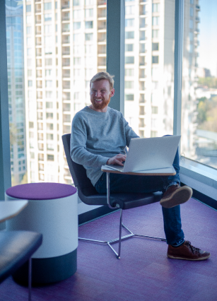 Male digital analytics expert smiling while working on laptop in front of window