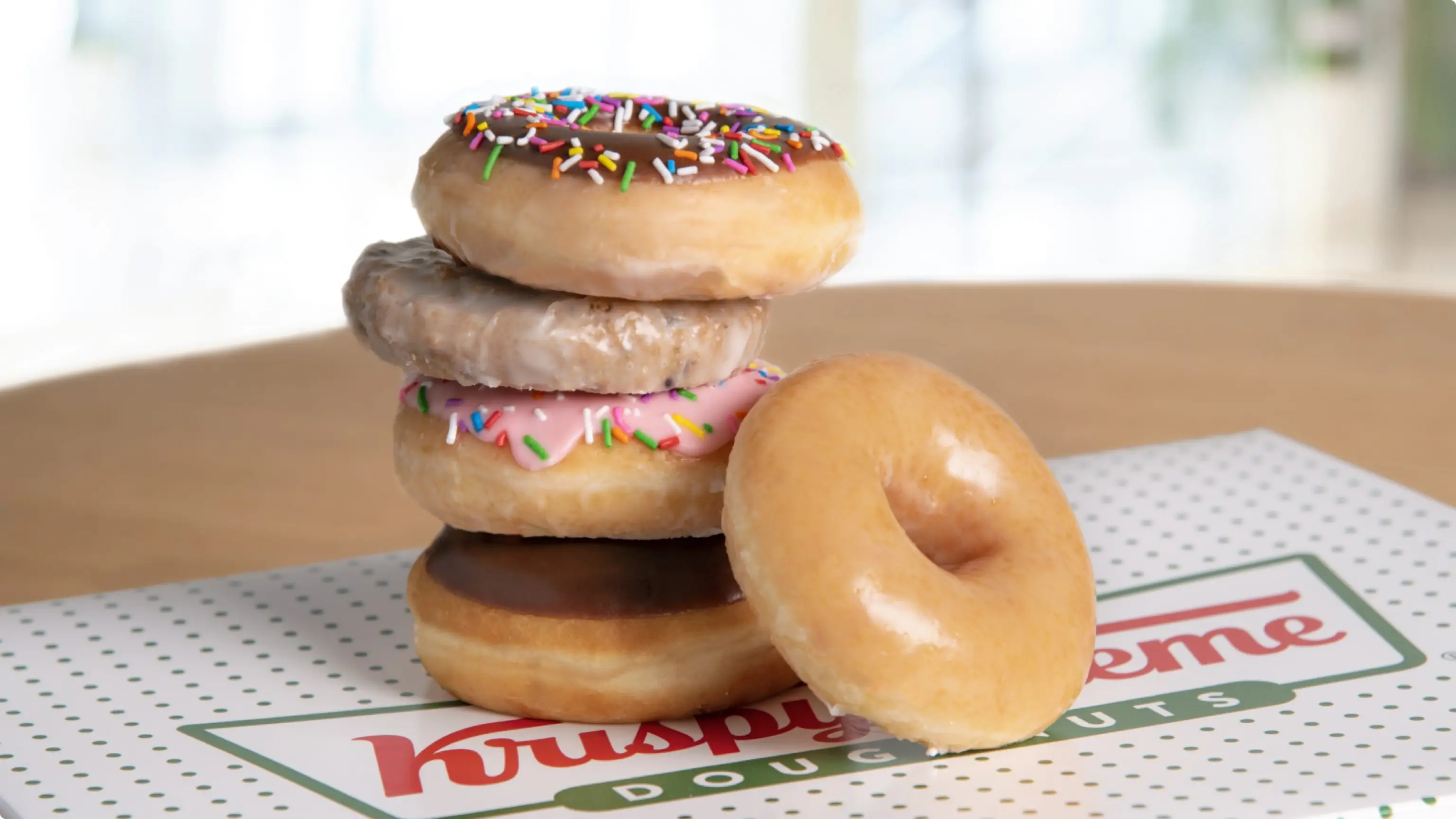 Stack of assorted Krispy Kreme doughnuts sitting on top of Krispy Kreme box.