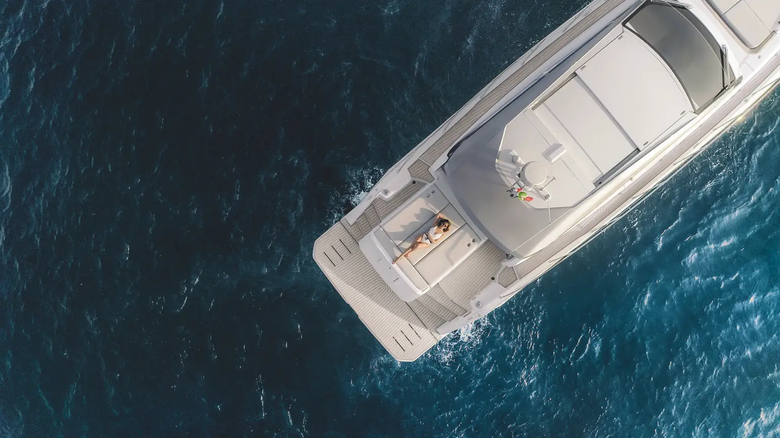 Aerial view of yacht cruising through the water with woman sunbathing.