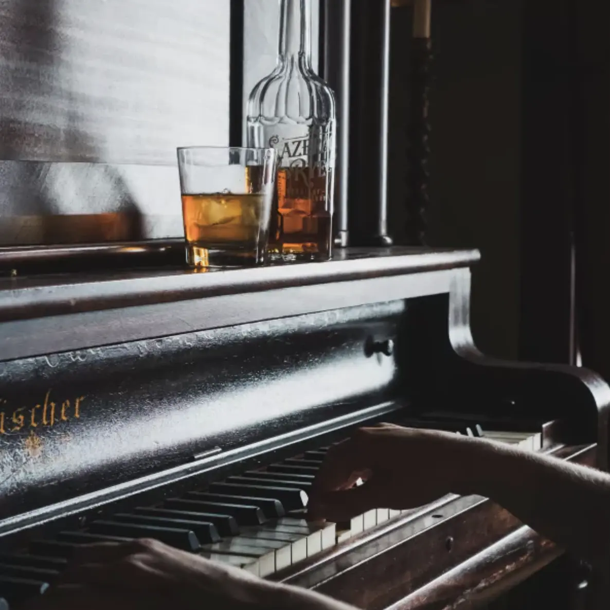 Person playing piano with whiskey glass on top for alt text example 
