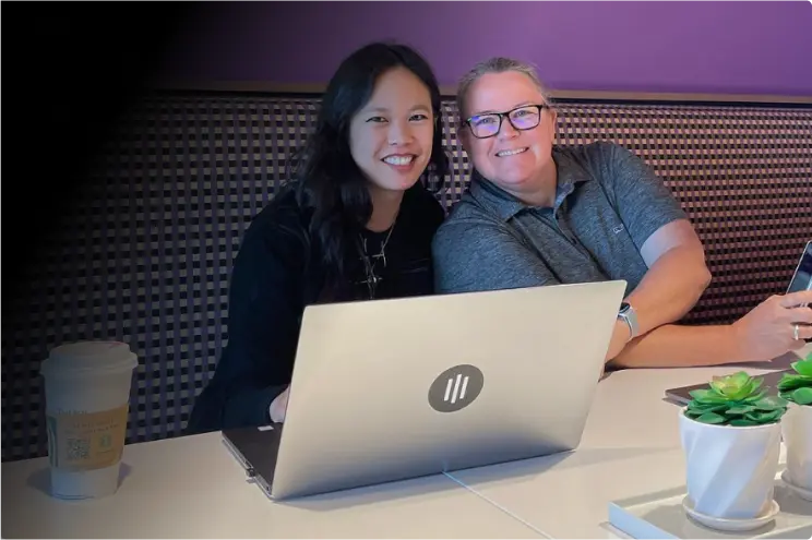 Two women smiling with laptop in front of them